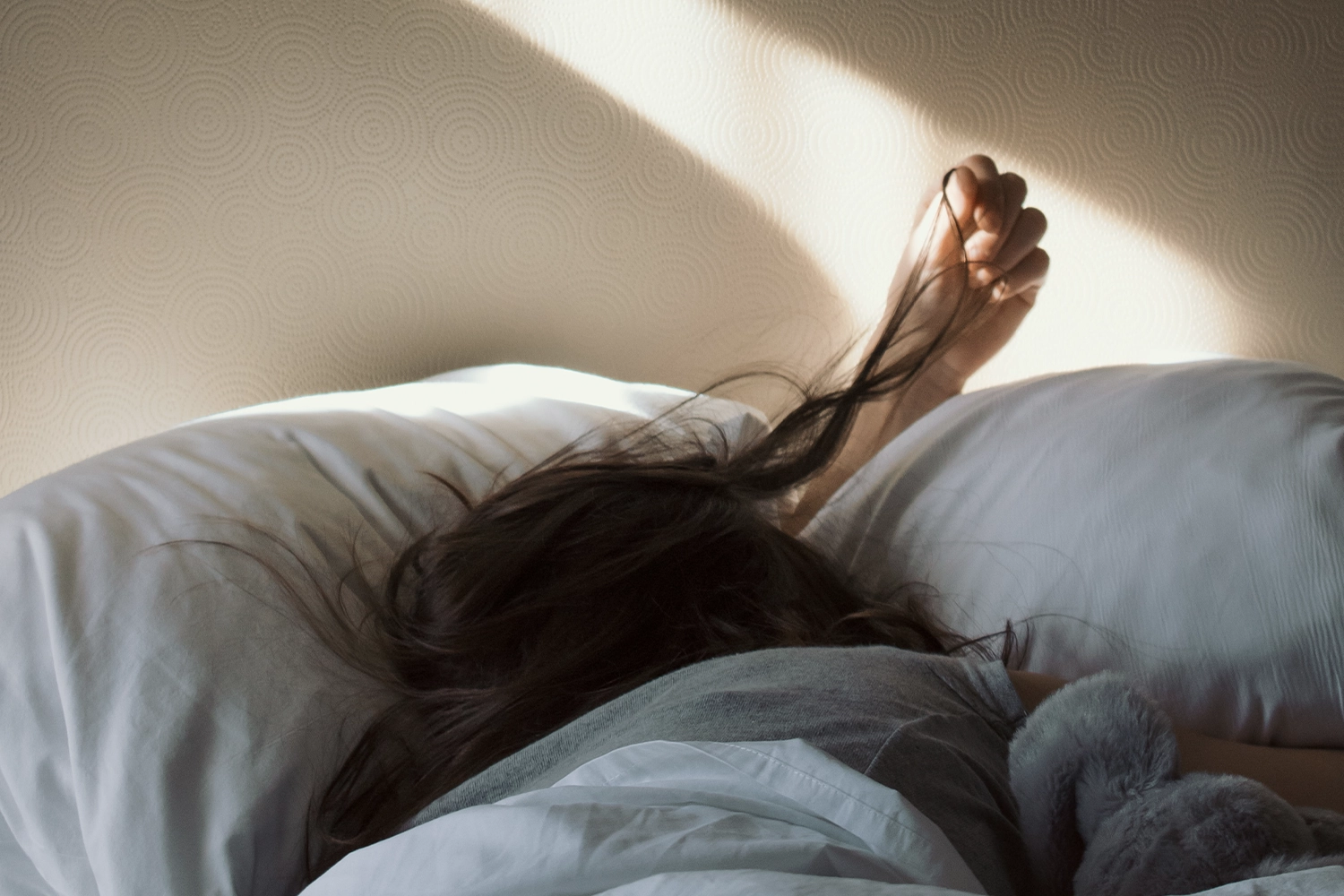 person under blanket in bed with hand running through hair